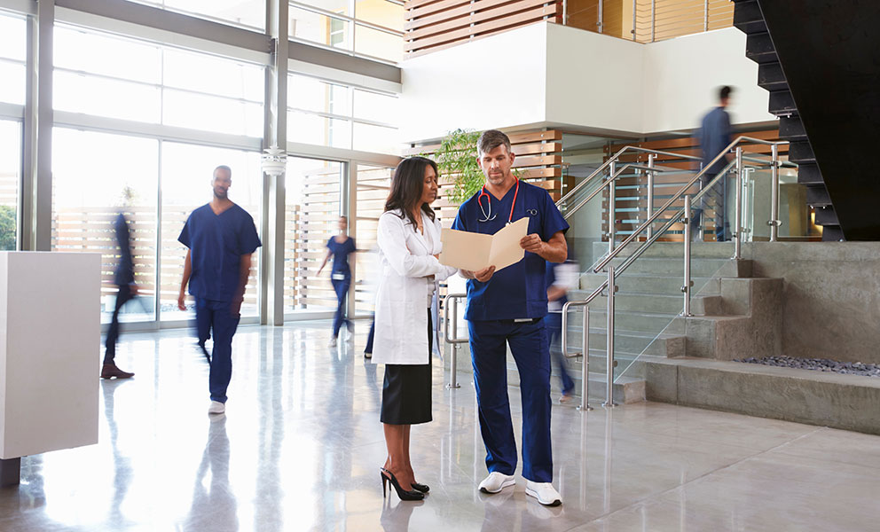 Two healthcare workers talk in the lobby of a busy hospital